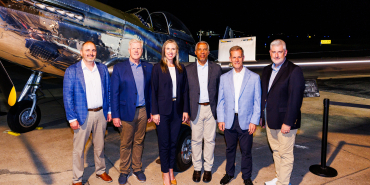 Six individuals pose for a photo in front of a vintage aircraft at night.